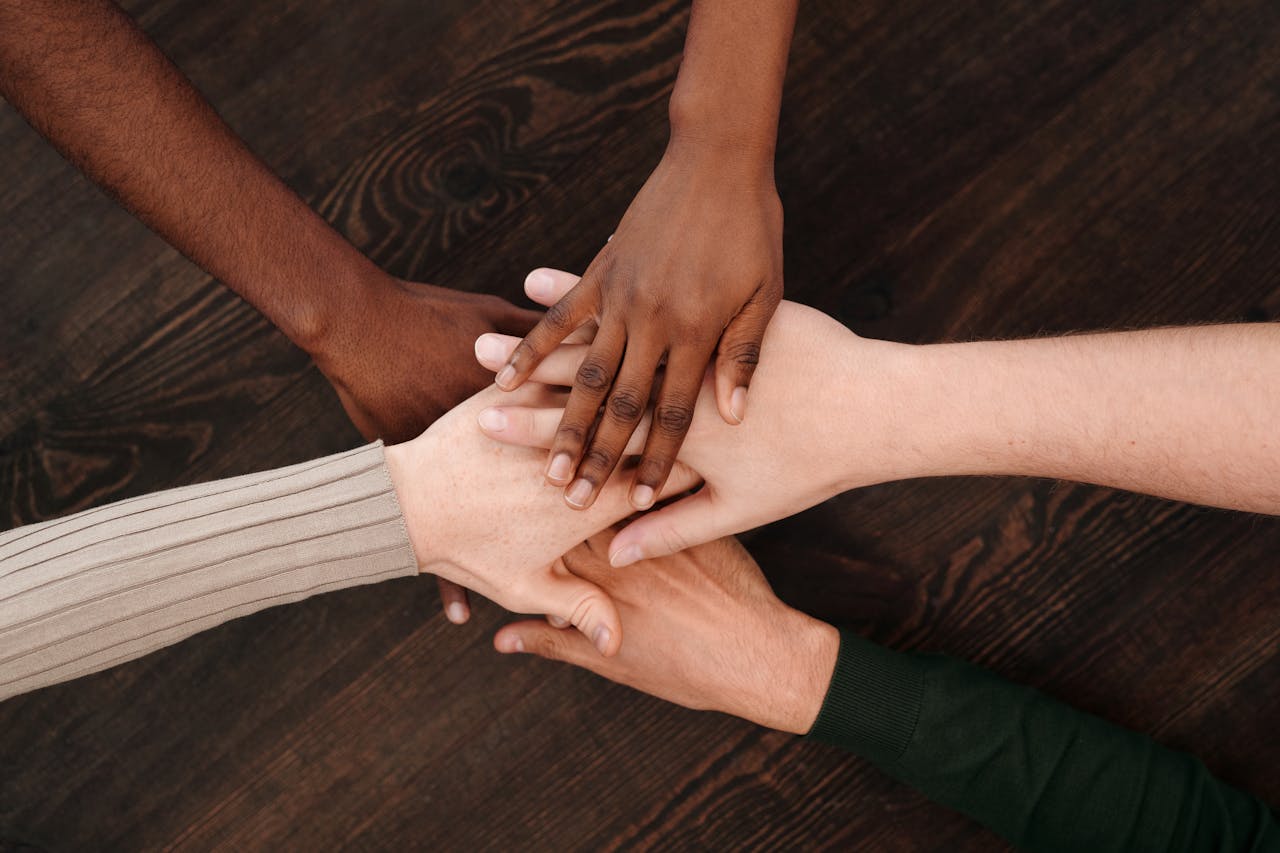 A diverse group of hands joining together, symbolizing unity and teamwork on a wooden surface.